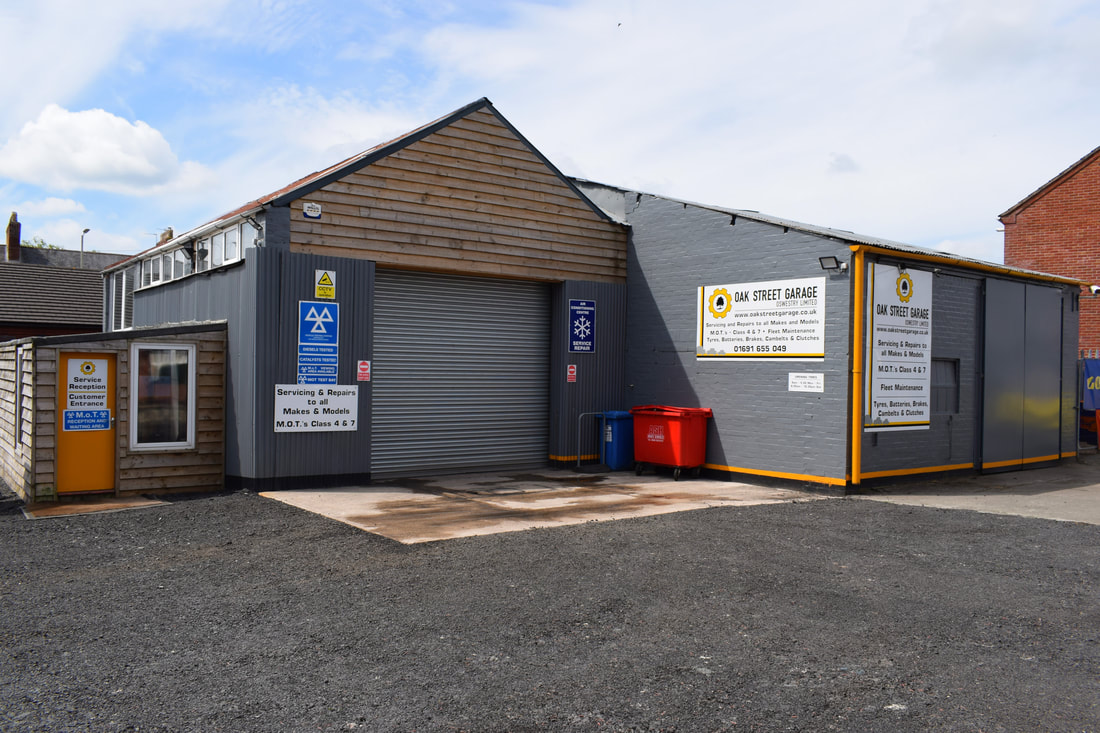 The front of Oak Street Garage with its yellow and white Oak Street Garage signs on the grey workshop